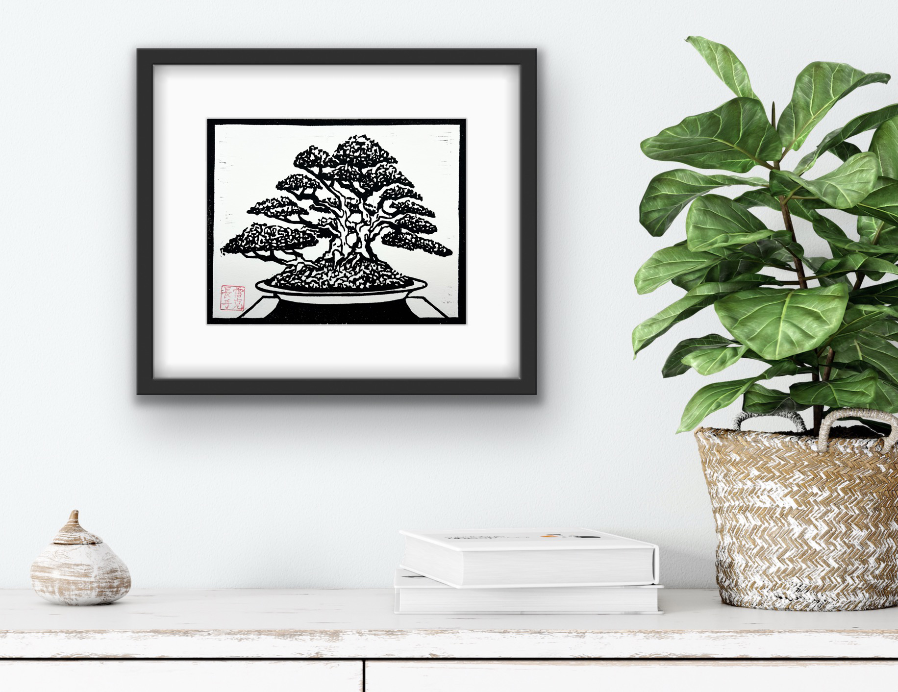 Framed Ota Azalea bonsai woodblock print by Ron Reekers displayed on a white wall above a console with books and a green indoor plant.