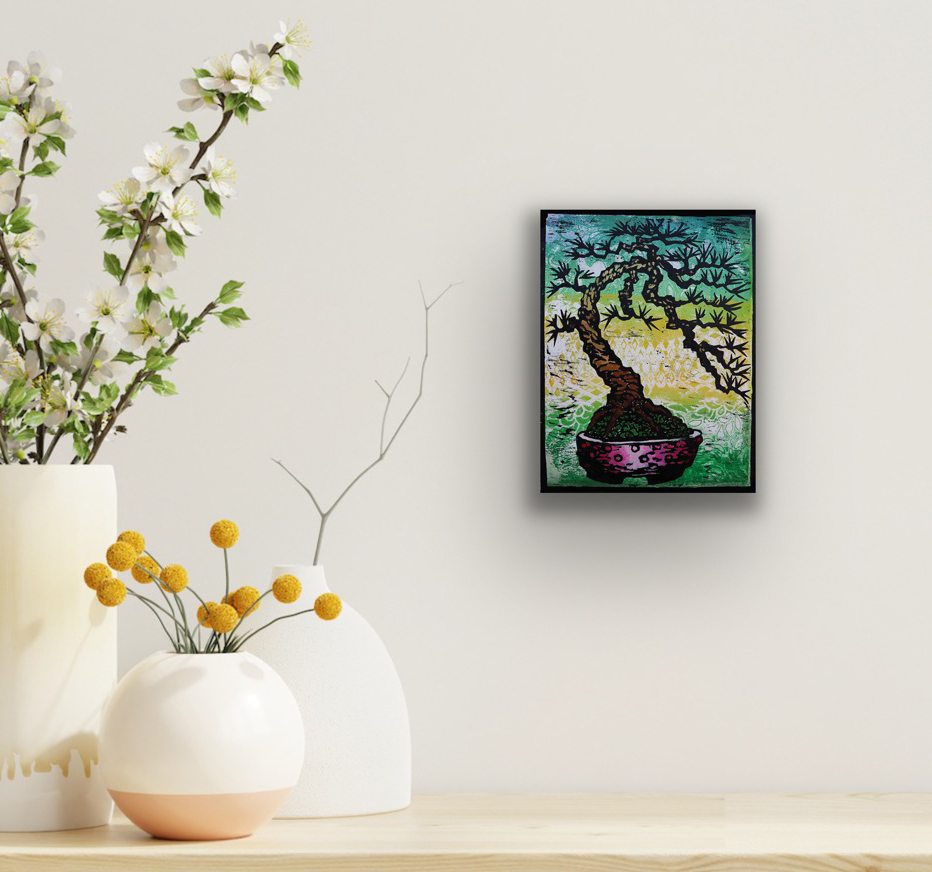 Bowing Pine original bonsai woodblock monoprint displayed in a black frame on a neutral wall above minimalist ceramic vases and floral arrangements.