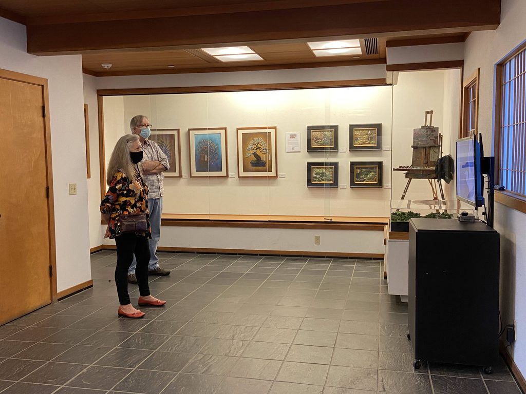 Two visitors viewing Ron Reekers' 2021 exhibition at the Japanese Friendship Garden & Museum in San Diego, featuring framed bonsai artwork and Japanese-inspired landscapes displayed in the gallery.